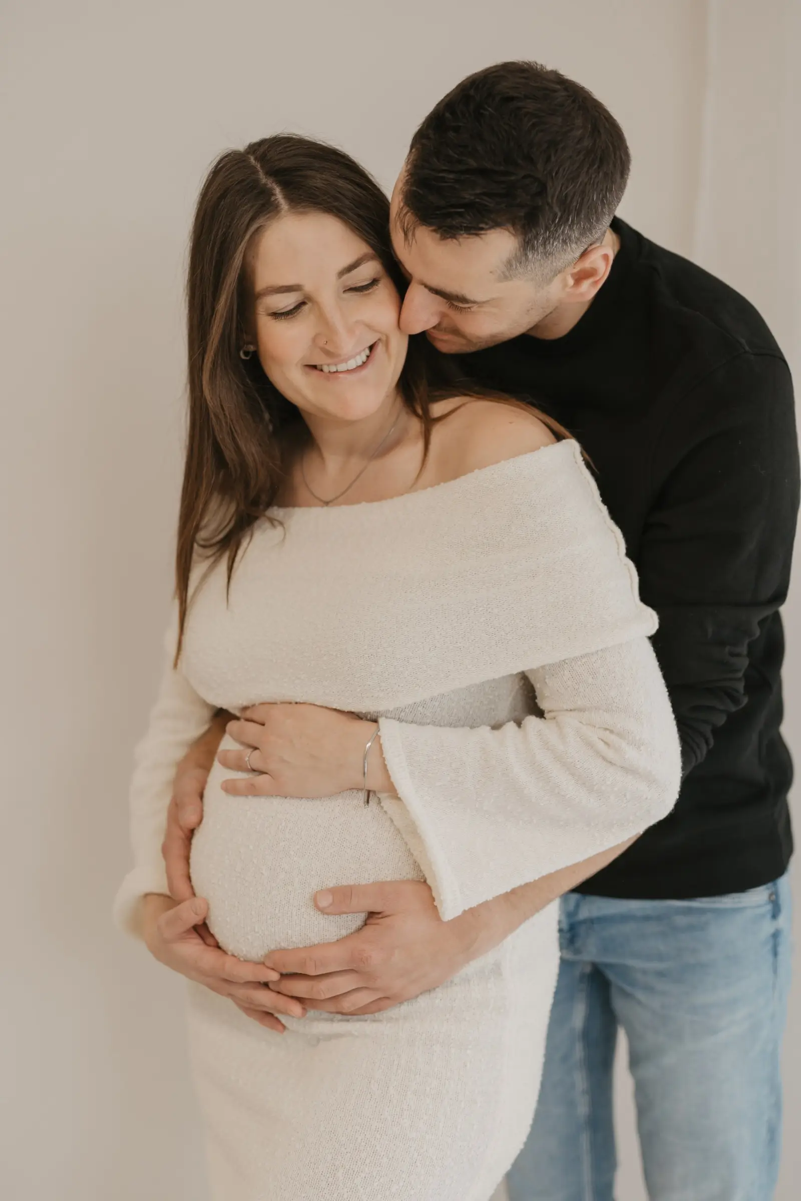 Werdende Eltern umarmen sich, Hände auf dem Babybauch