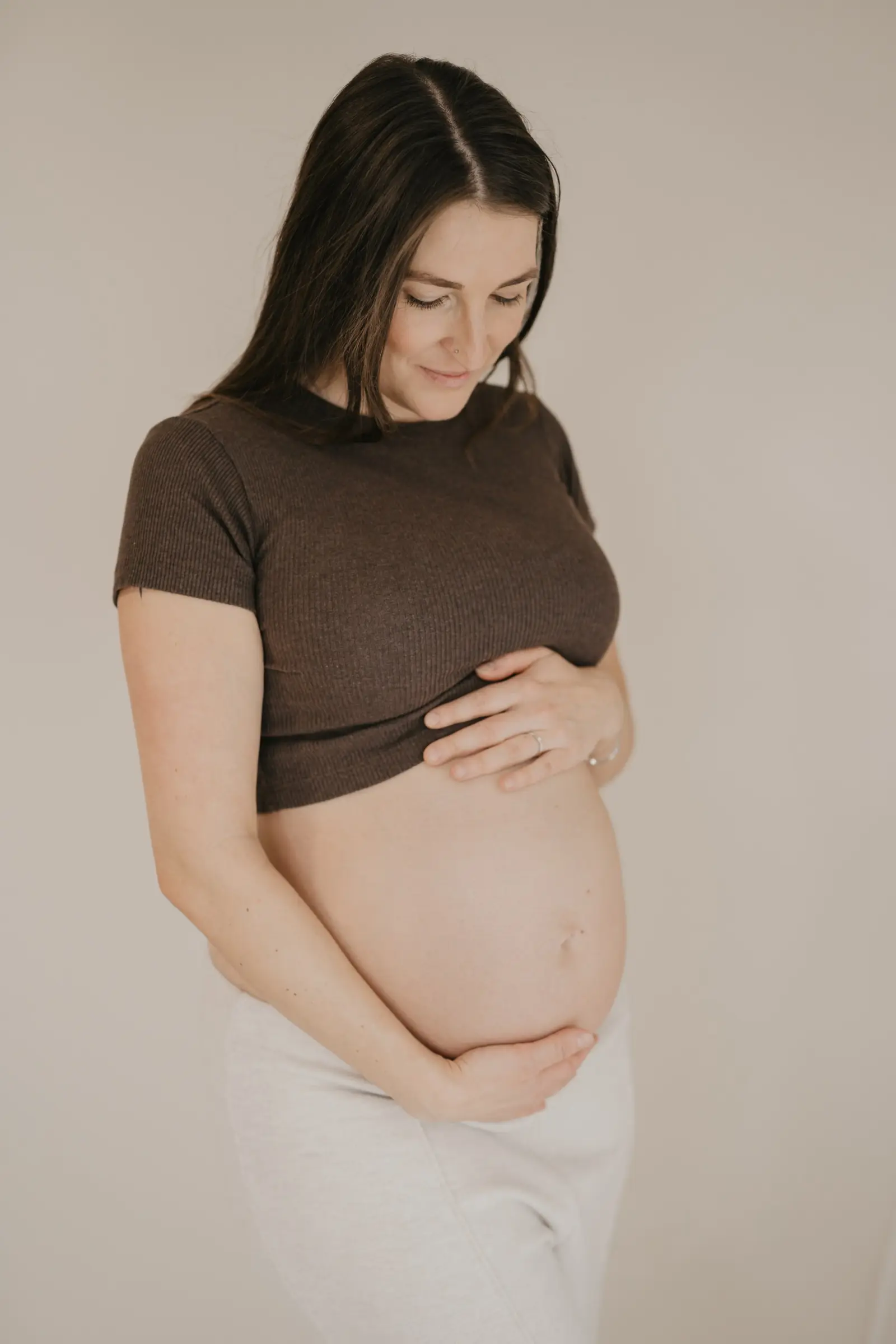 Schwangere im braunen Top, Hände auf dem Babybauch