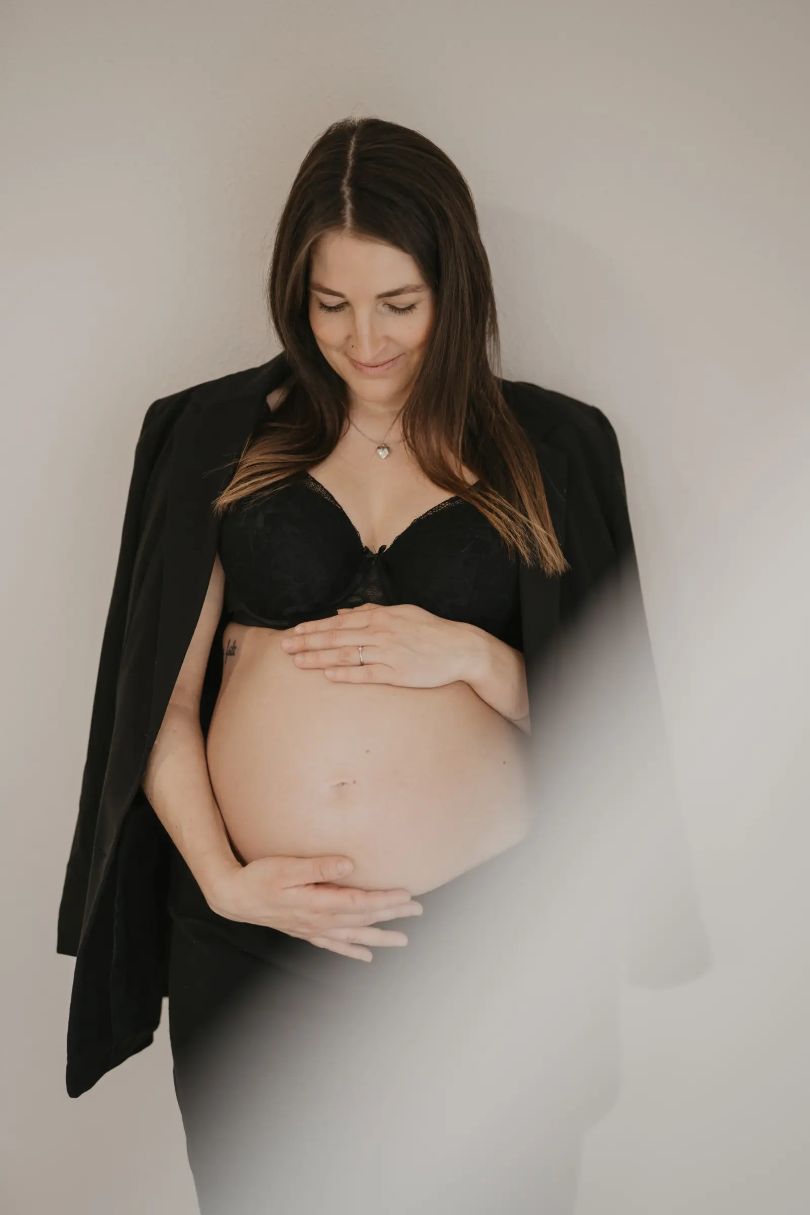 Schwangere im schwarzen Blazer, Hände auf dem Babybauch