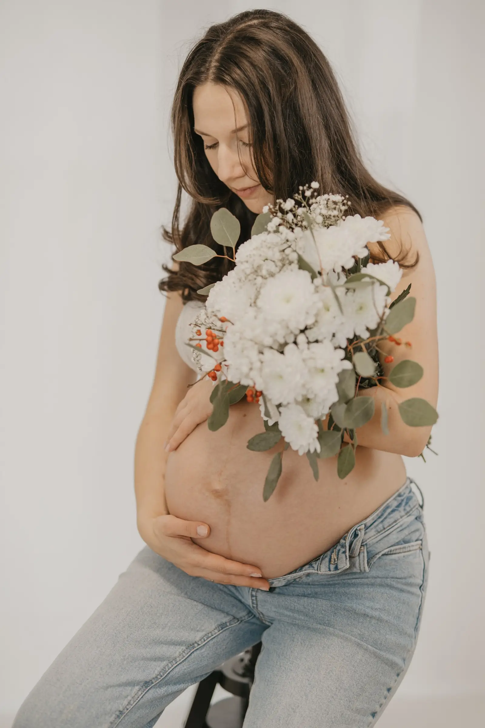 Schwangere mit weißem Blumenstrauß vor dem Babybauch